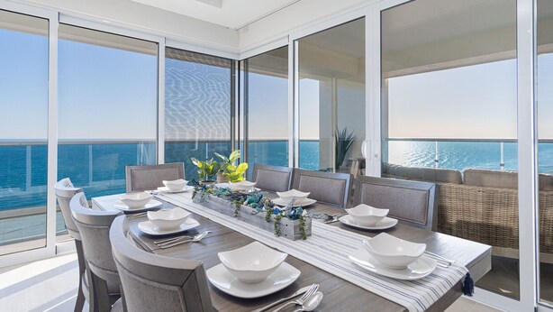 A dining area with a view of the sea, featuring a long table set for six, large windows, and a balcony with wicker furniture. - Impressive & Beautiful 3 Bedroom end Unit Ocean Front Encantame C-1901 (Puerto Peñasco)