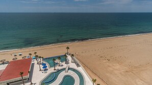 An aerial view of a beach resort with a swimming pool, palm trees, and a sandy beach. - Amazing Condo by the Beach Encantame W1203 (Puerto Peñasco)