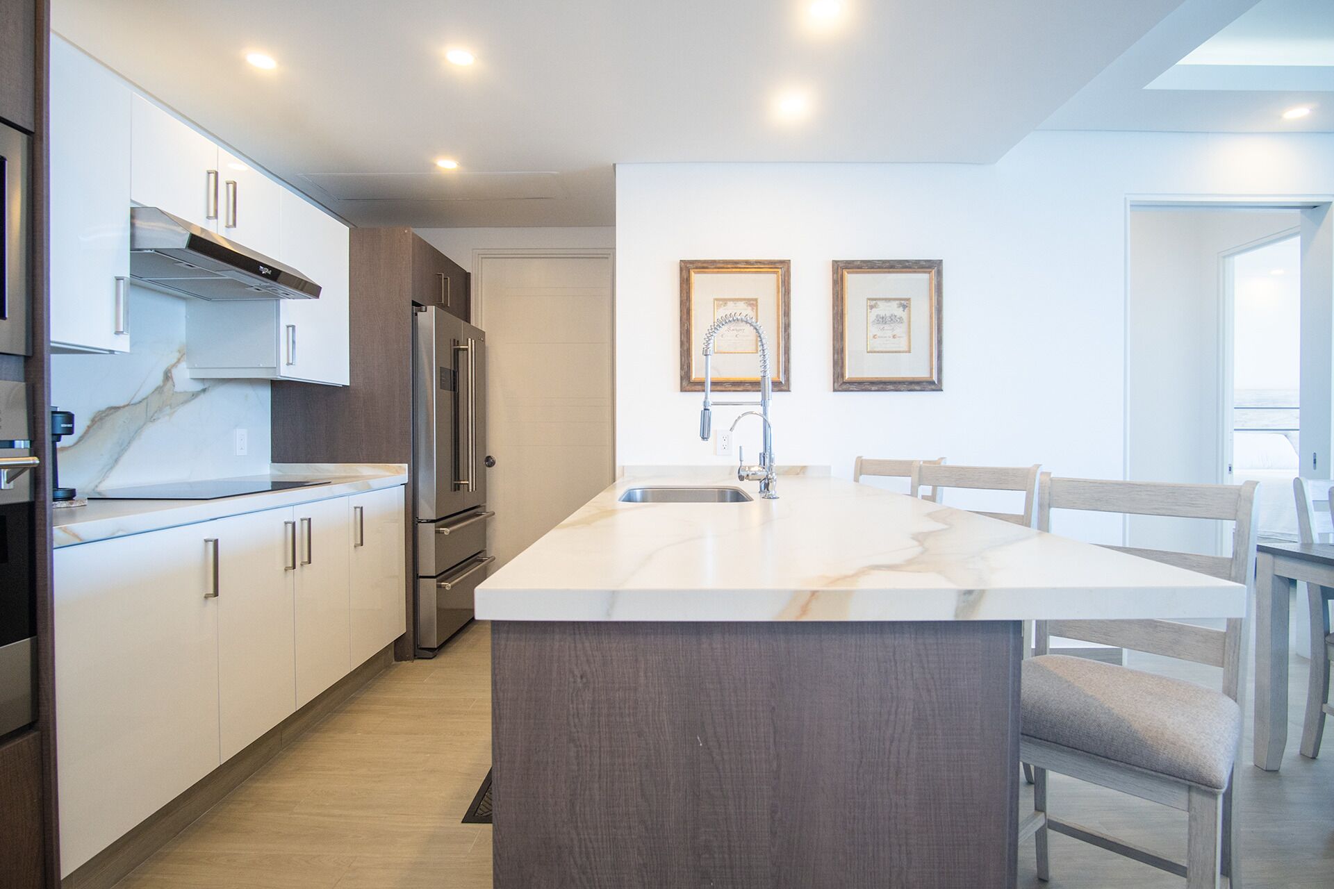 A modern kitchen with a central island, stainless steel appliances, and a dining area with wooden chairs.