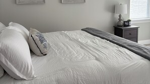 Una camera da letto con un letto, cuscini, un comodino, una lampada e due quadri appesi al muro.