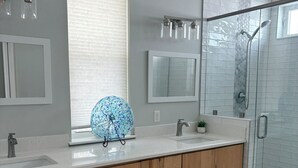 Un bagno moderno con un mobile bagno in legno, due lavabi, una cabina doccia in vetro e una ciotola decorativa sul ripiano.