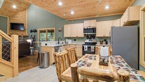 A kitchen with wooden cabinets, a microwave, a refrigerator, and a dining table with a placemat. - Jones Creek Cove | Private Hot Tub (Sevierville)