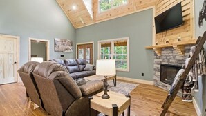 A living room with a leather sectional sofa, a wooden coffee table, a fireplace, and a TV mounted on the wall. - Jones Creek Cove | Private Hot Tub (Sevierville)