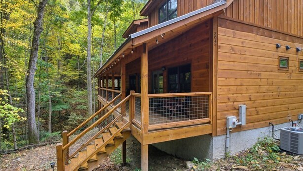 A wooden cabin with a covered porch and a staircase leading to the entrance. - Jones Creek Cove | Private Hot Tub (Sevierville)
