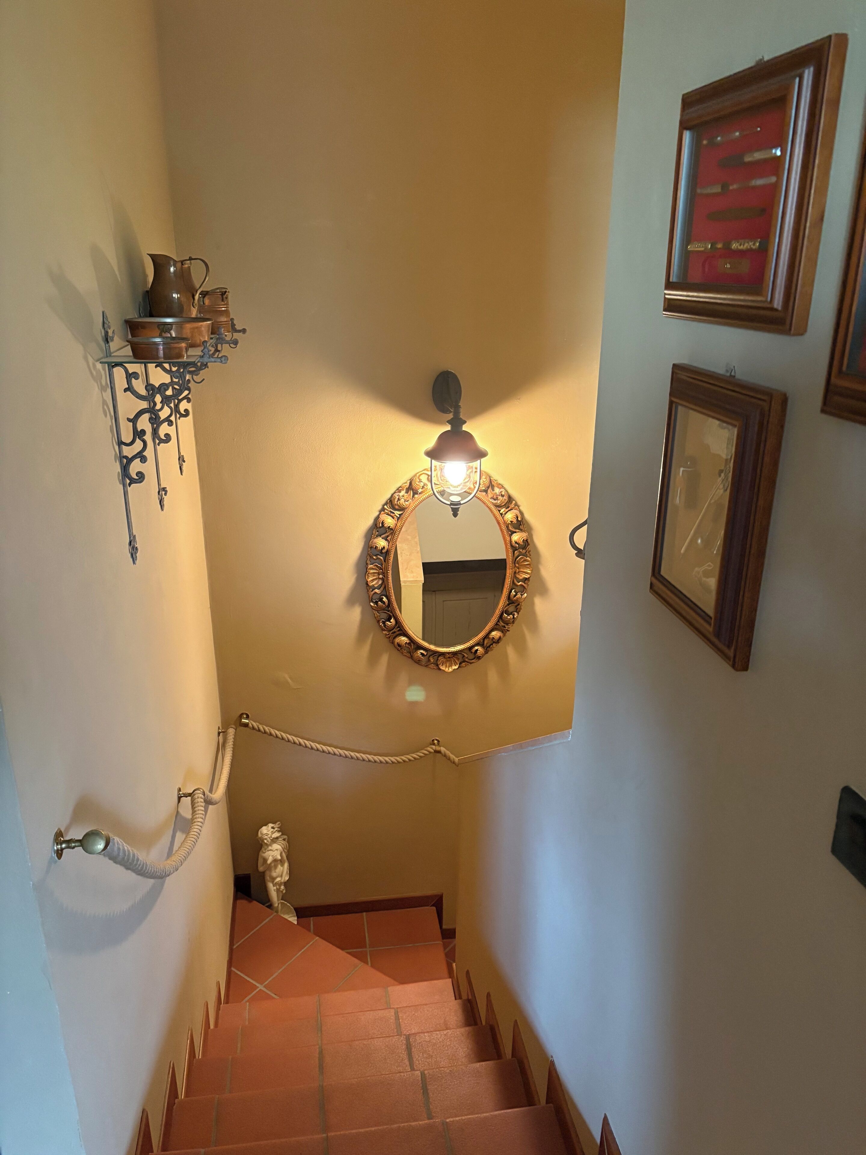 A staircase with a handrail, a wall-mounted mirror, and a light fixture.