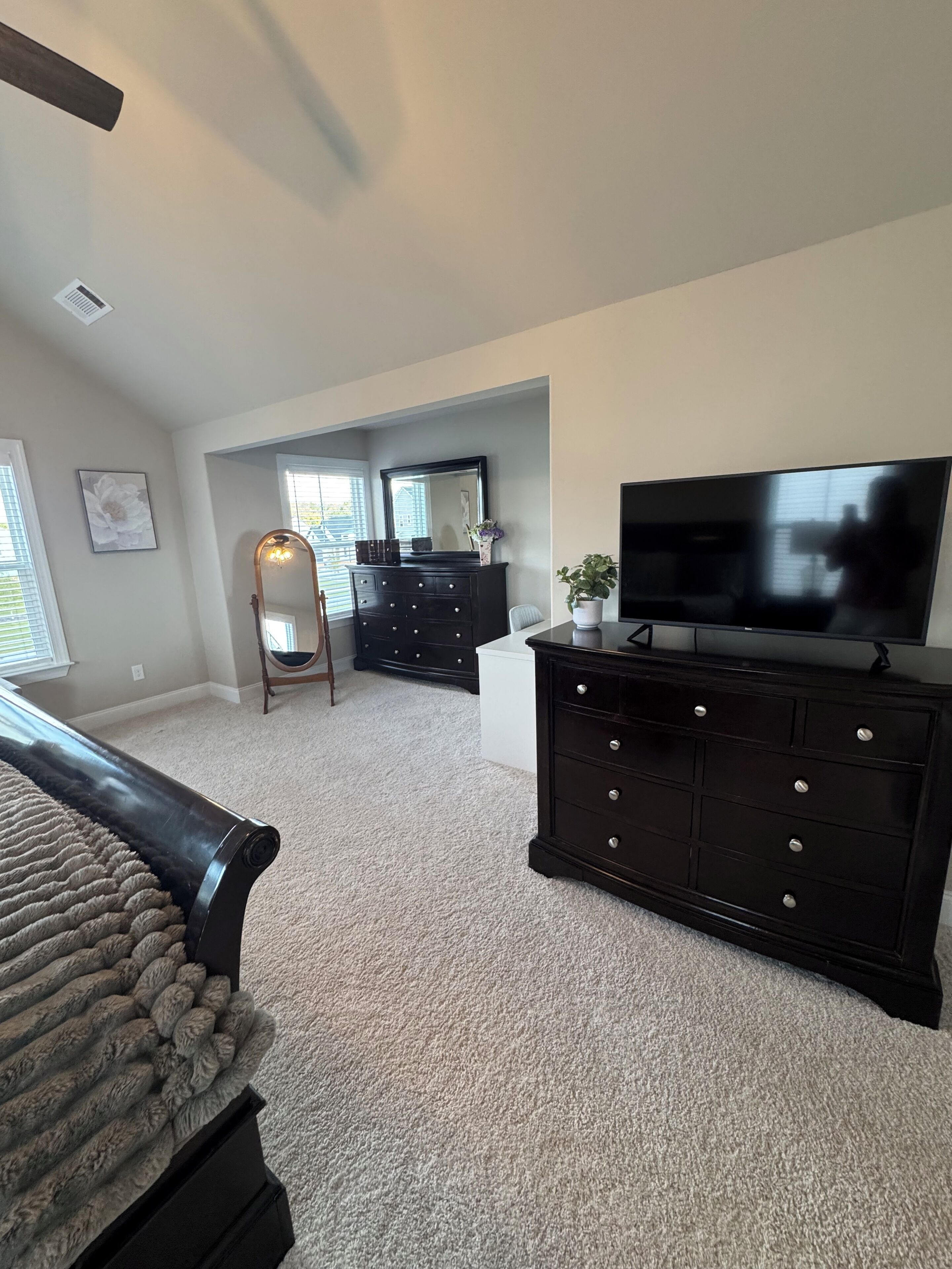 A spacious living room with a large flat-screen TV, dark wooden dresser, and a cozy area rug.