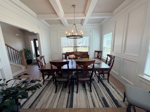 A dining area with a wooden table, chairs, a chandelier, and a view through the window.