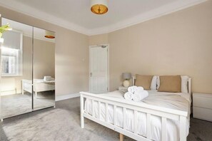 Un dormitorio con cama, mesita de noche, espejo, puerta y ventana.