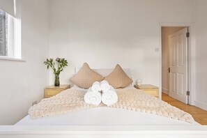 A bedroom with a bed, two nightstands, a vase with flowers, and a door.