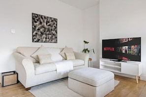 Una sala moderna con un sofá, un reposapiés y un televisor de pantalla plana mostrando Netflix.