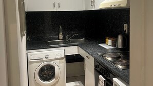 A compact kitchen with white cabinets, a washing machine, a stove, and a sink. - Nice 1-bedroom apartment in Namur (Namur)