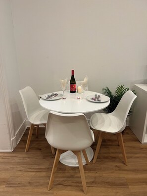Ett runt matbord med vita stolar, en vinflaska och ett ljus.