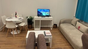 A living room with a white desk, a TV, a sofa, and a dining table set with plates and a wine bottle. - Nice 1-bedroom apartment in Namur (Namur)