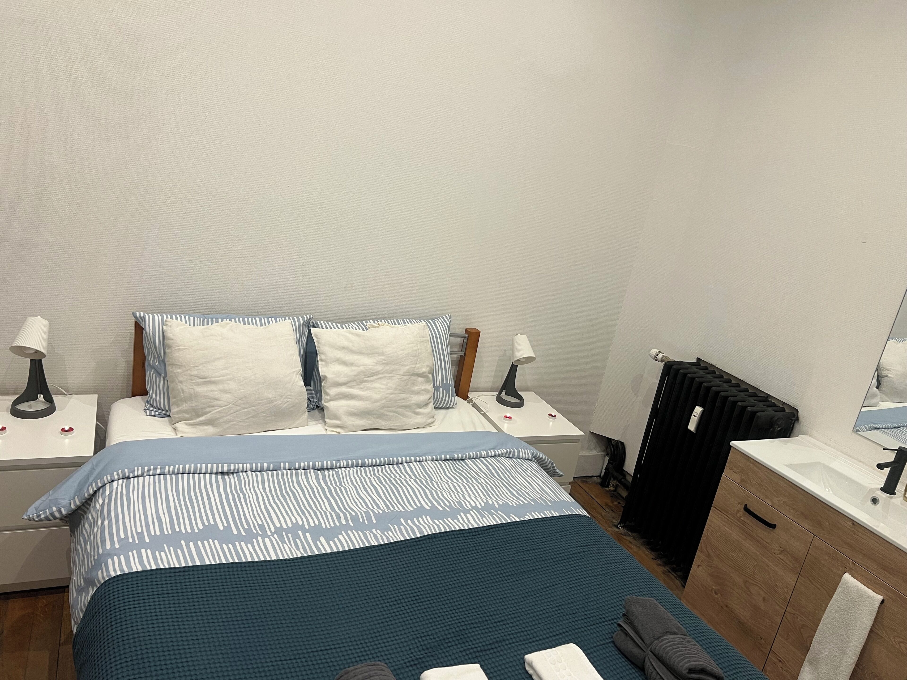 A neatly arranged bedroom with a bed, two bedside tables, a radiator, and a wooden cabinet.