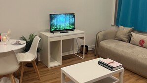 A living room with a TV on a white desk, a sofa, a coffee table, and a dining area with chairs and a table. - Nice 1-bedroom apartment in Namur (Namur)