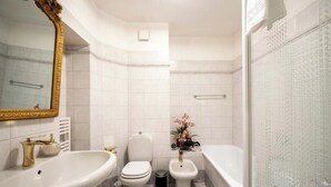 A bathroom with a large mirror, two sinks, a toilet, a bidet, and a bathtub.