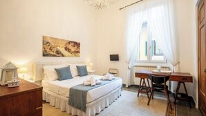 A bedroom with a bed, bedside table, lamp, and a desk with a chair.