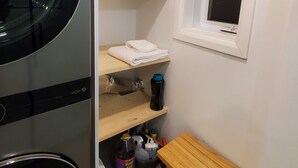 A compact kitchen with a built-in refrigerator, a microwave, and a sink. There are wooden shelves above the sink and a small wooden table beside it. A window with a black blind is visible on the wall. - Superb apartment near Longueuil metro station (Longueuil)