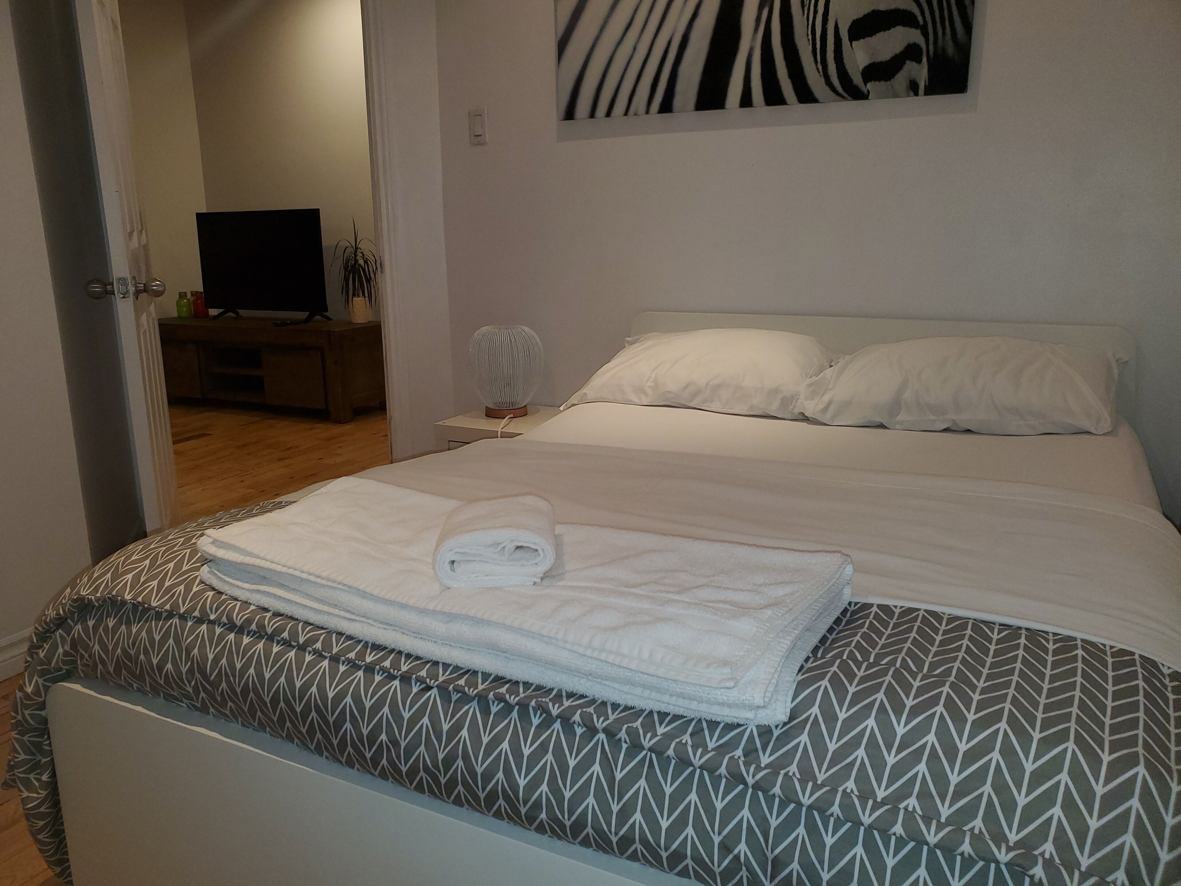 A neatly made bed with a patterned bedspread, a rolled towel, and a wall-mounted zebra print.