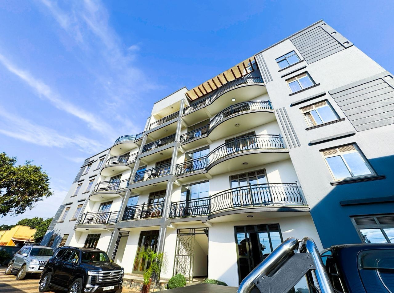 Un edificio residencial de varios pisos con balcones, una zona de estacionamiento y un cielo azul despejado.