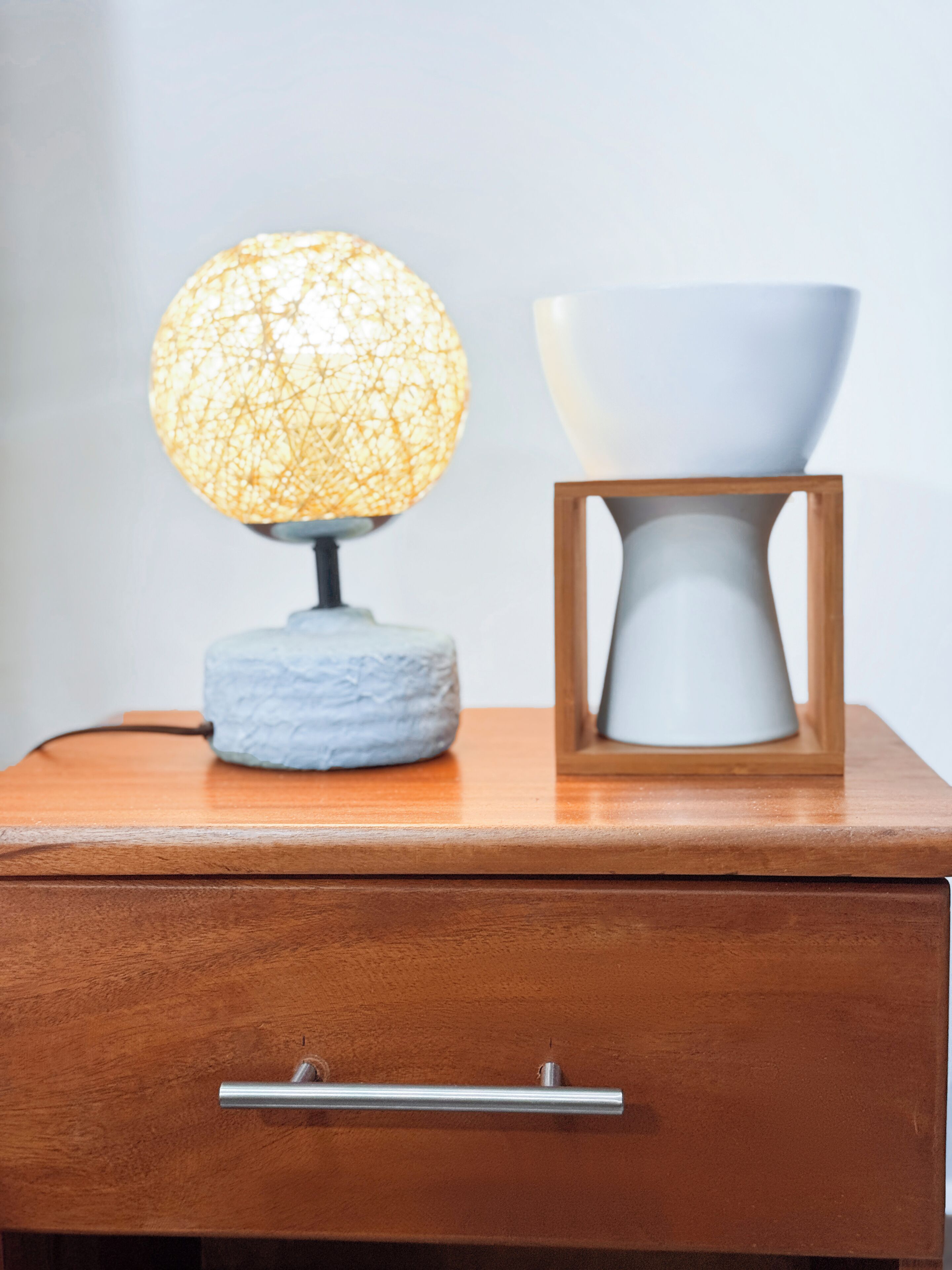 Ein Nachttisch aus Holz mit einer Lampe und einer weißen Vase darauf.