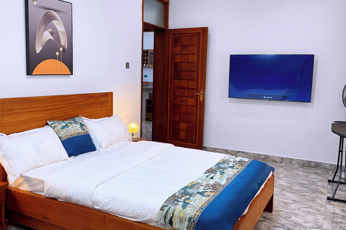 Une chambre à coucher avec un lit en bois, un téléviseur fixé au mur et une porte donnant sur une autre pièce.