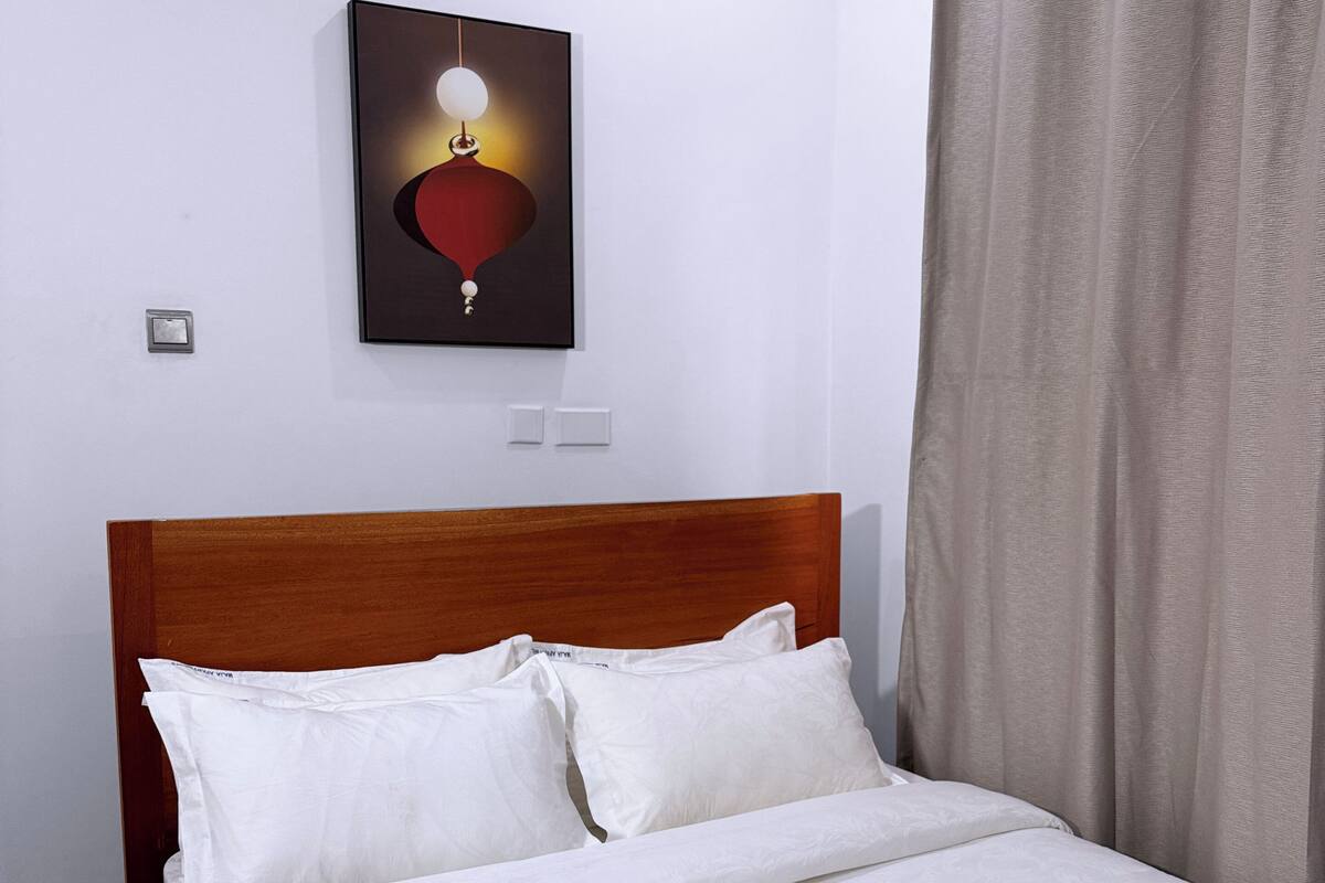 Un lit bien fait, avec du linge de lit blanc, dans une chambre dont la tête de lit est en bois.