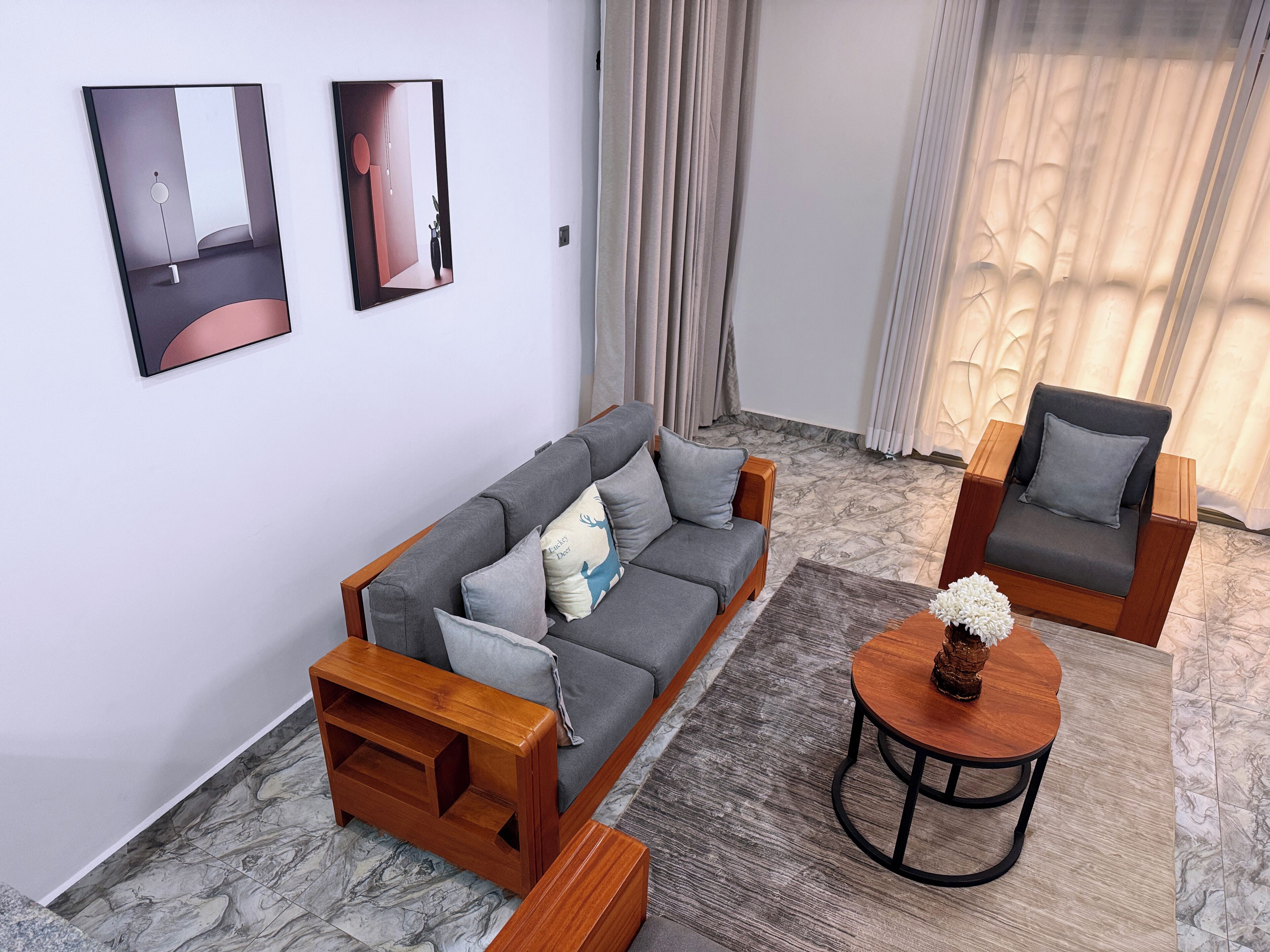 A modern living room with a grey sofa, two armchairs, a wooden coffee table, and a marble floor.