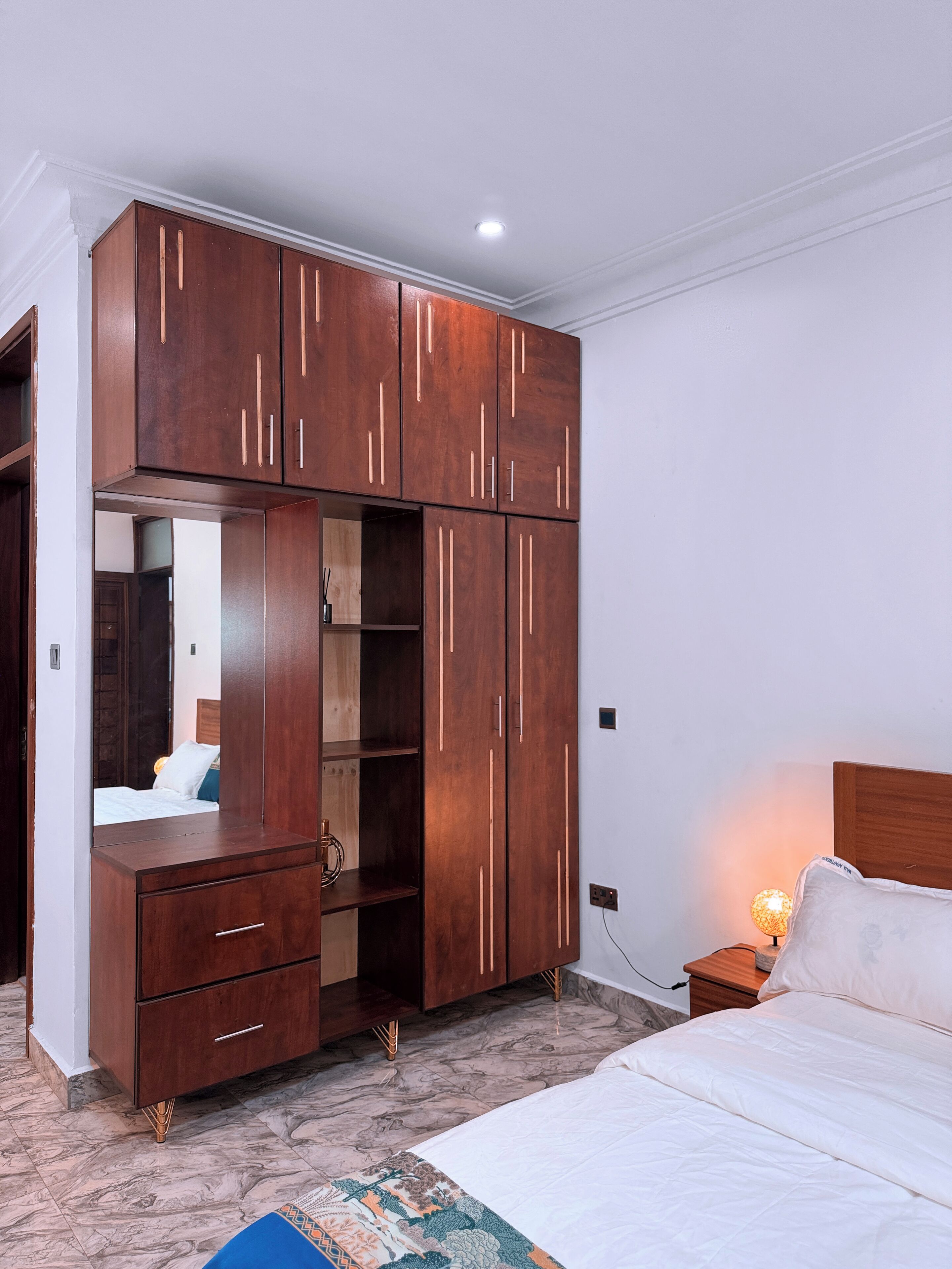 A bedroom with a large wooden wardrobe, a bed, and a nightstand with a lamp.