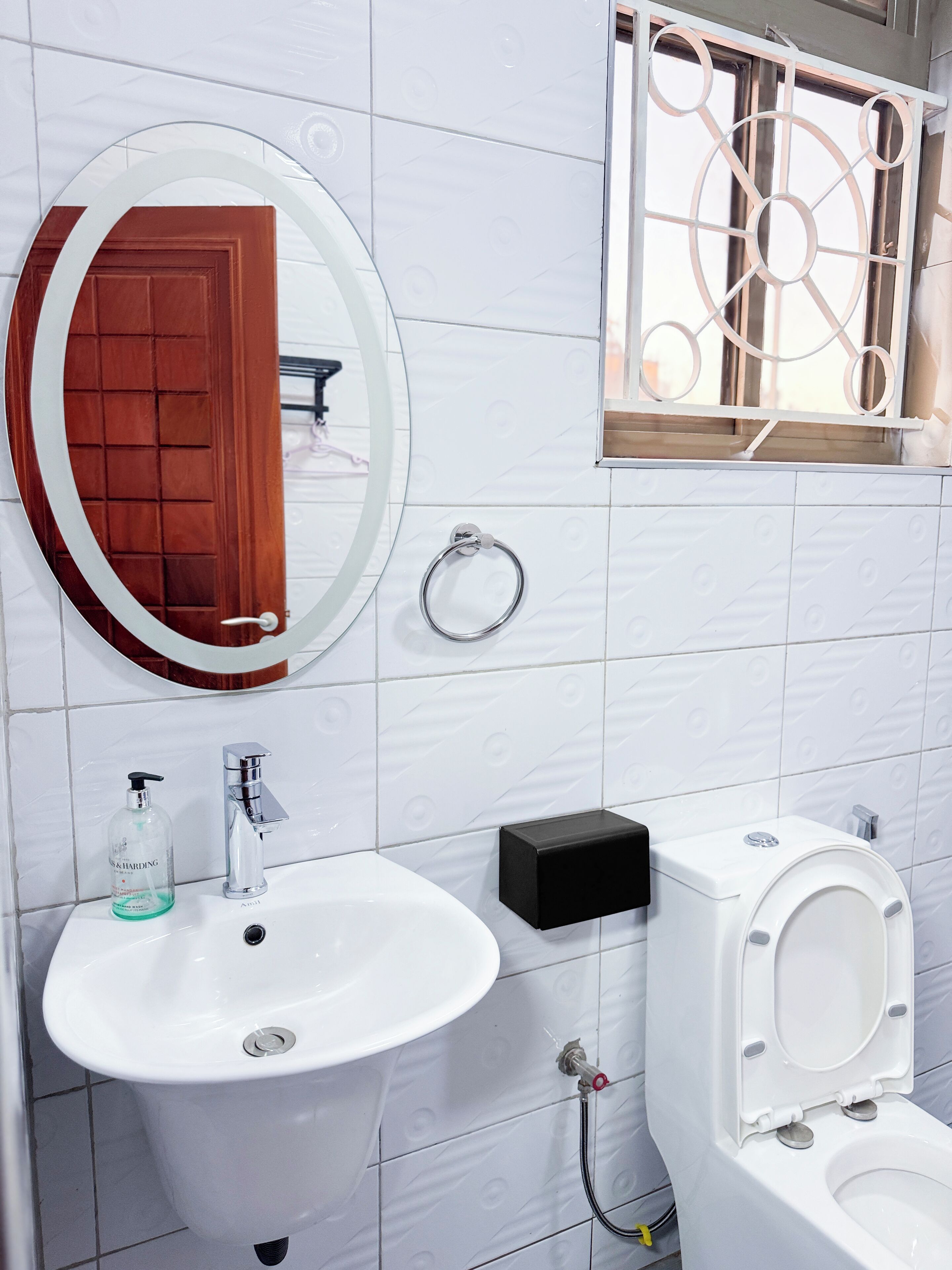 A bathroom with a white sink, a mirror with a wooden frame, a toilet, and a window with a metal grille.