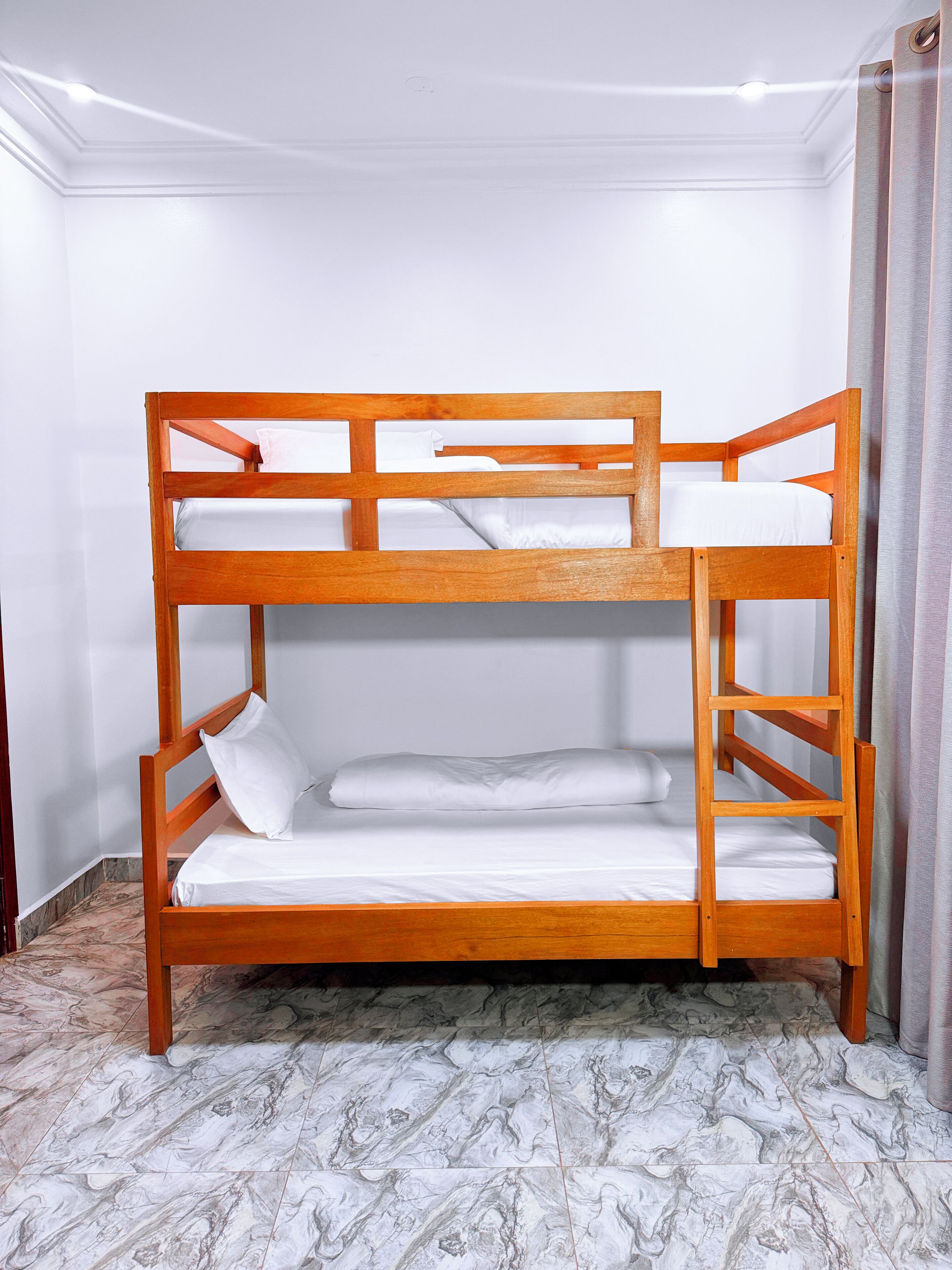 A bunk bed with two levels, white bedding, and a marble-patterned floor.