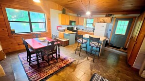 A cozy kitchen with wooden cabinets, a dining table with chairs, and a large window providing a view of the outdoors.