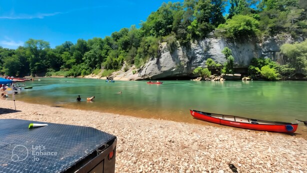 A river with boats, a rocky cliff, and a beach with a tent.