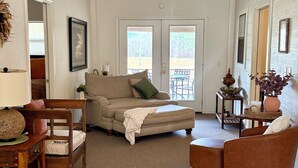 Ein geräumiges Wohnzimmer mit einem beigefarbenen Sofa, einem Holzstuhl, einem braunen Sessel und einem kleinen Tisch mit Dekoration.