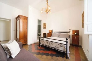 A bedroom with a metal bed frame, a wooden wardrobe, a chandelier, and a patterned floor.