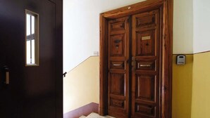 A wooden double door with a small window, a doormat, and a wall-mounted device. - BuddyRent - Vatican Domus - 4 ospiti (Rome)