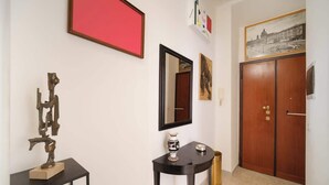 A hallway with a sculpture, a mirror, a framed photograph, and a wooden door. - BuddyRent - Vatican Domus - 4 ospiti (Rome)