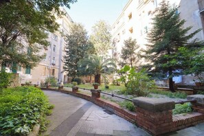 A courtyard with a brick pathway, greenery, and buildings with balconies.