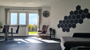 A modern living room with a sofa, a dining table with chairs, a wall clock, and a hexagonal wall decoration. - M&M AusZeit in Schwabenländle in Winterlingen (Winterlingen)
