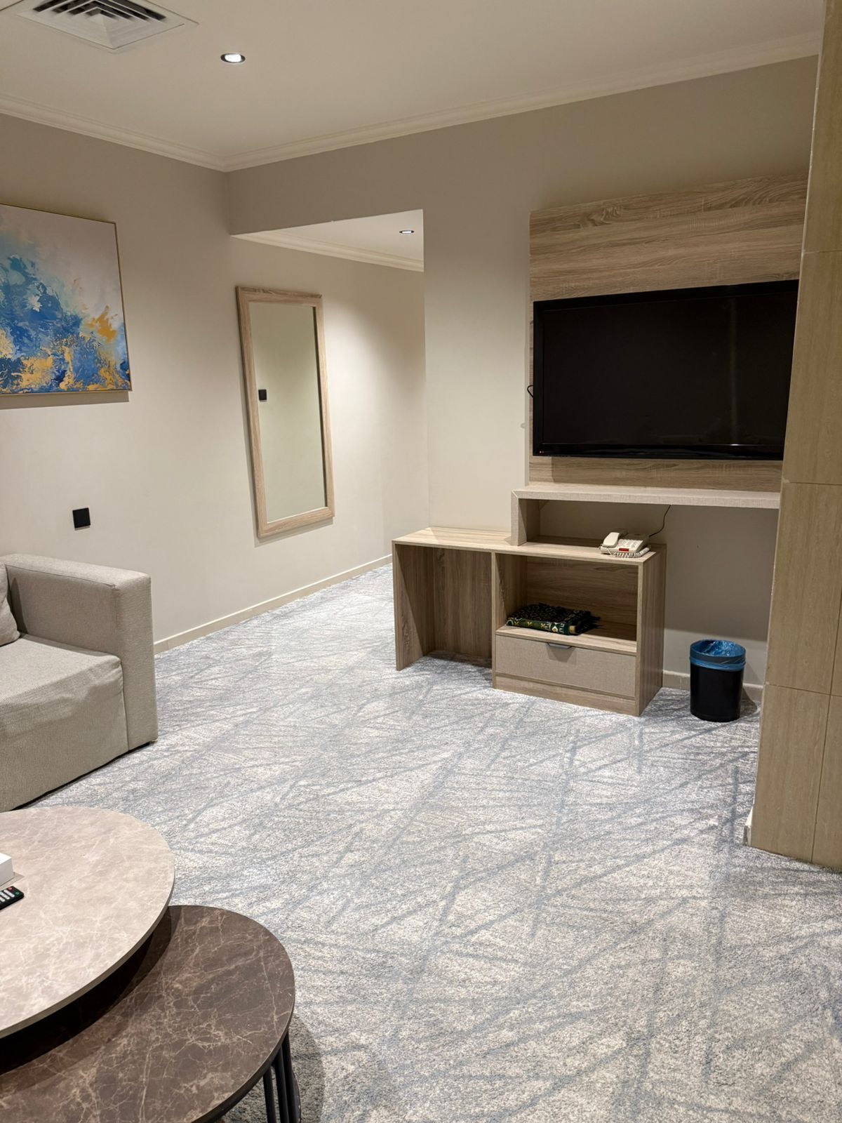 Un salon moderne avec un canapé, une table ronde, un téléviseur fixé à un mur en bois et un tapis à motifs.