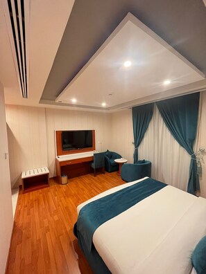 A modern hotel room with a bed, a desk, a chair, a television, and a small table. - Villa park (Al Khobar)