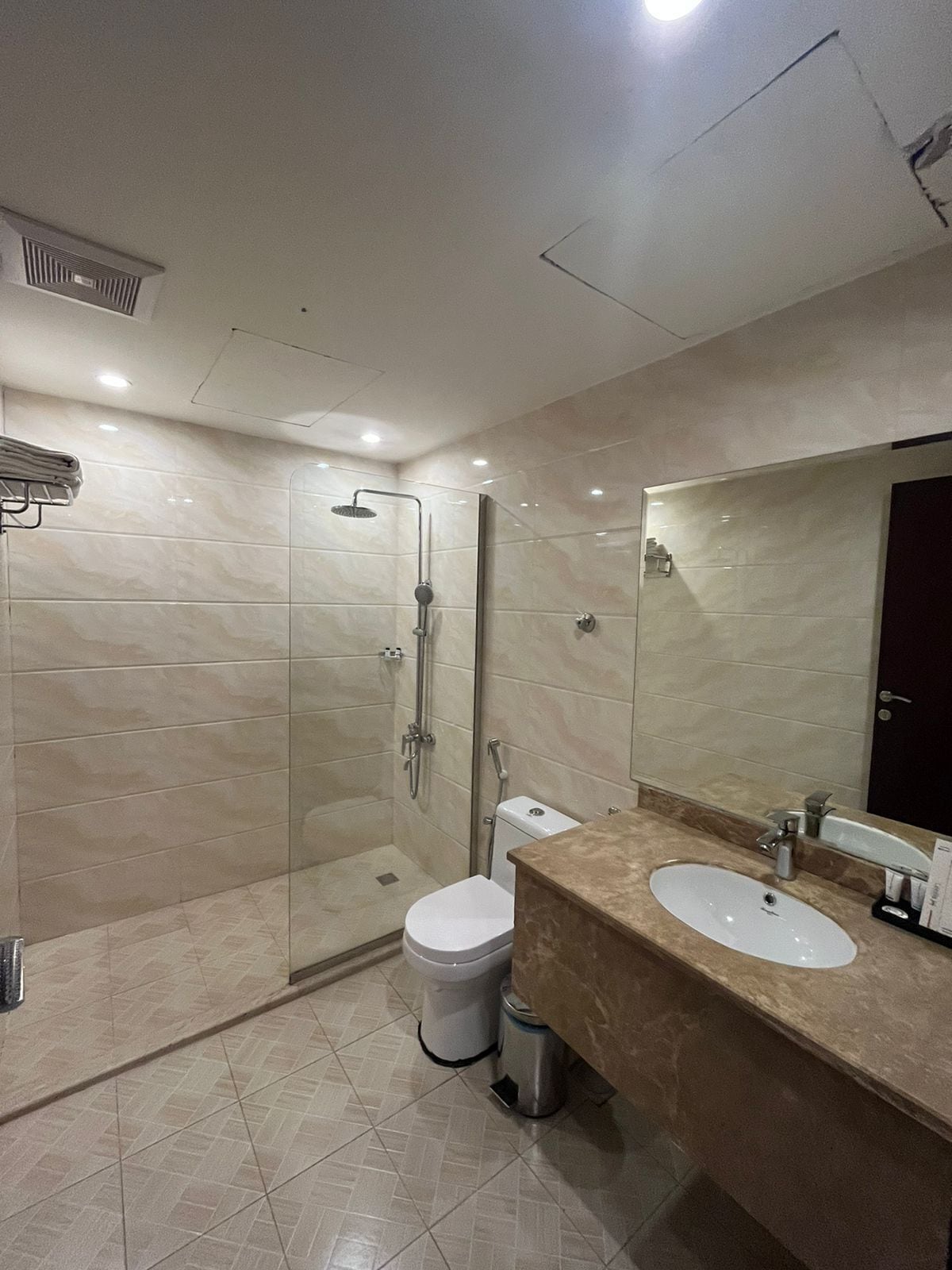 A modern bathroom with a glass-enclosed shower, a white toilet, a sink with a marble countertop, and a large mirror.