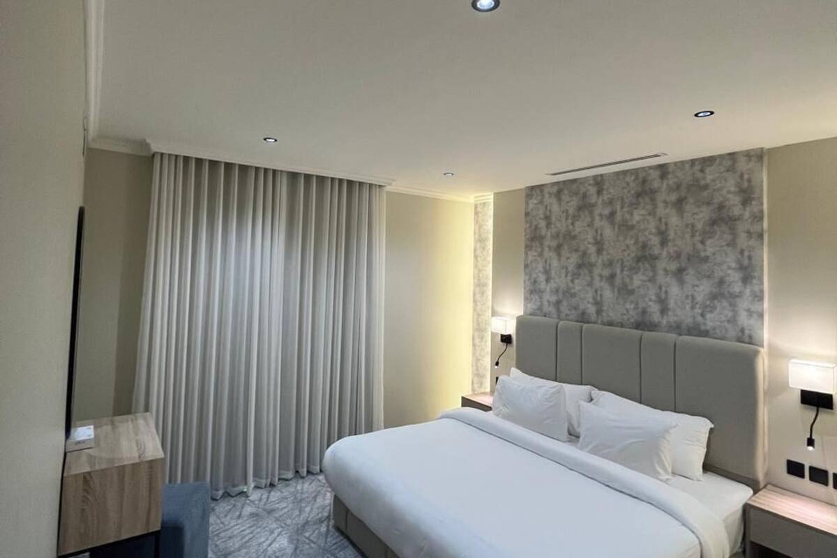 Una habitación de hotel moderna con una cama grande, una mesita de noche, una lámpara y un ventanal con cortinas.