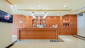 A reception desk with a wooden finish, a digital screen, and a clock on the wall. - Villa park (Al Khobar)