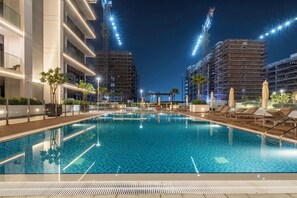 Una piscina con sillas de descanso y sombrillas, rodeada de edificios modernos y grúas de construcción.