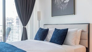 Camera d'albergo moderna con un letto grande, una testiera, una lampada da comodino e vista sulla città dalla finestra.