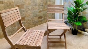 Un conjunto de banco y silla de madera frente a una pared de piedra, con una planta en maceta cerca.