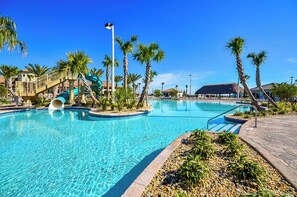 A swimming pool with a water slide, palm trees, and a thatched-roof building.