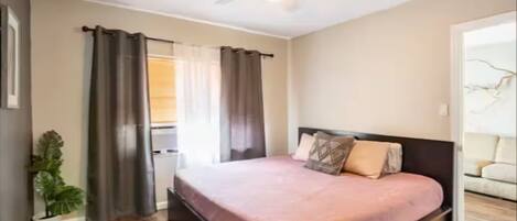 A bedroom with a bed, curtains, a ceiling fan, and a potted plant.