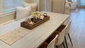 A dining area with a long table, white chairs, and a decorative centerpiece. - Seas the Day 30A - 6 Seater Golf Cart, 2 Pools, Beach Chairs, Wi-Fi & AC (Panama City Beach)